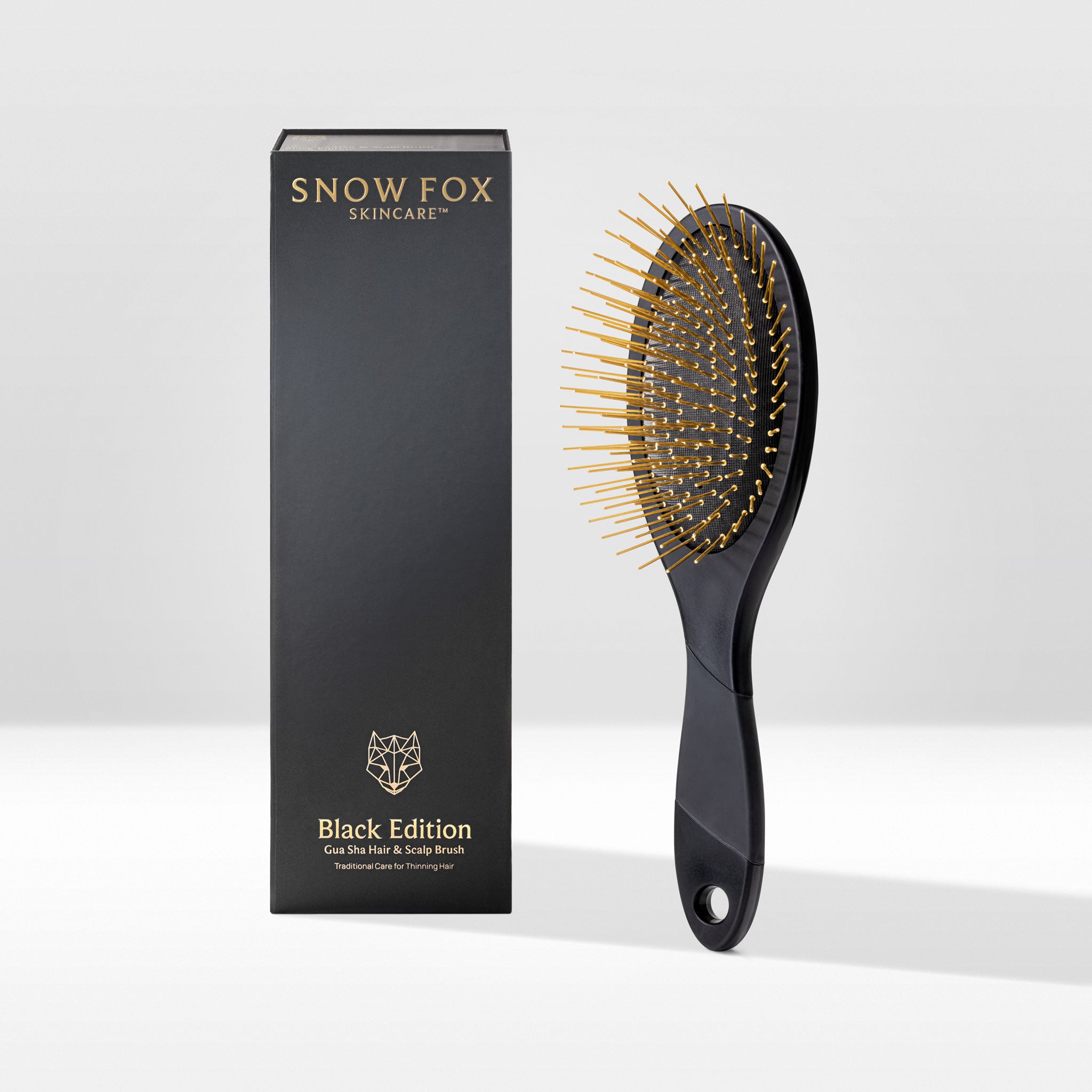 Black Edition Gua Sha brush by Snow Fox Skincare with black handle and gold acupressure needles on a white background