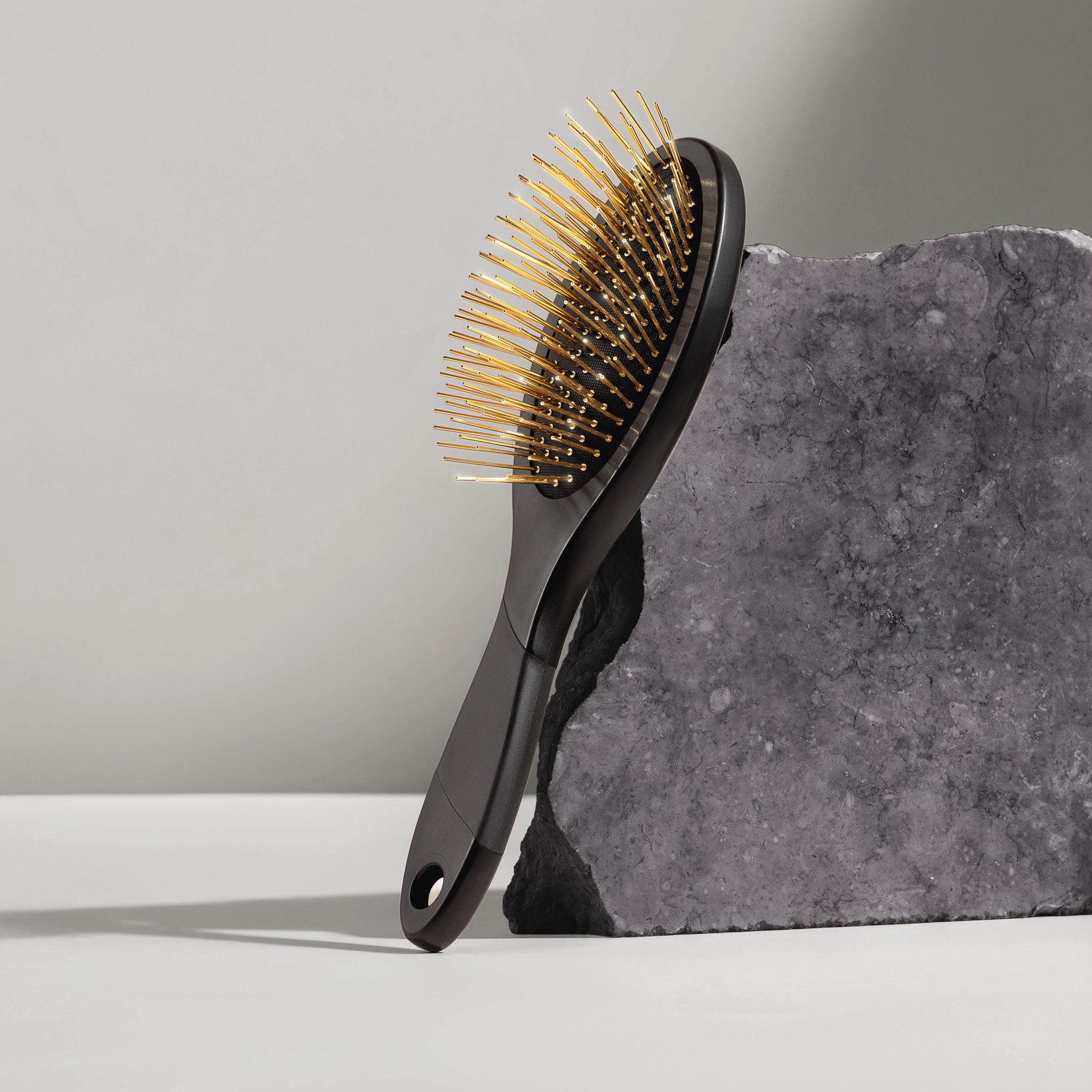 Black Gua Sha brush with gold acupressure needles on a gray stone slab
