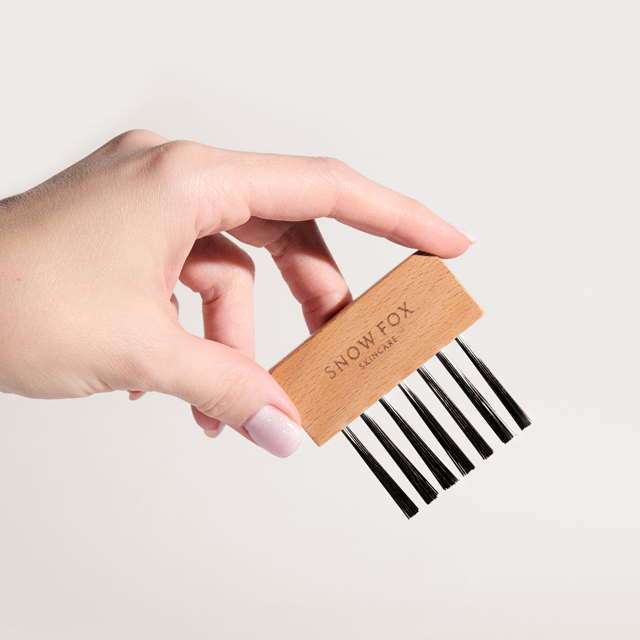a woman's hand holding the Snow Fox Skincare Gua Sha Brush Cleaning Kit bristile comb on a light beige background