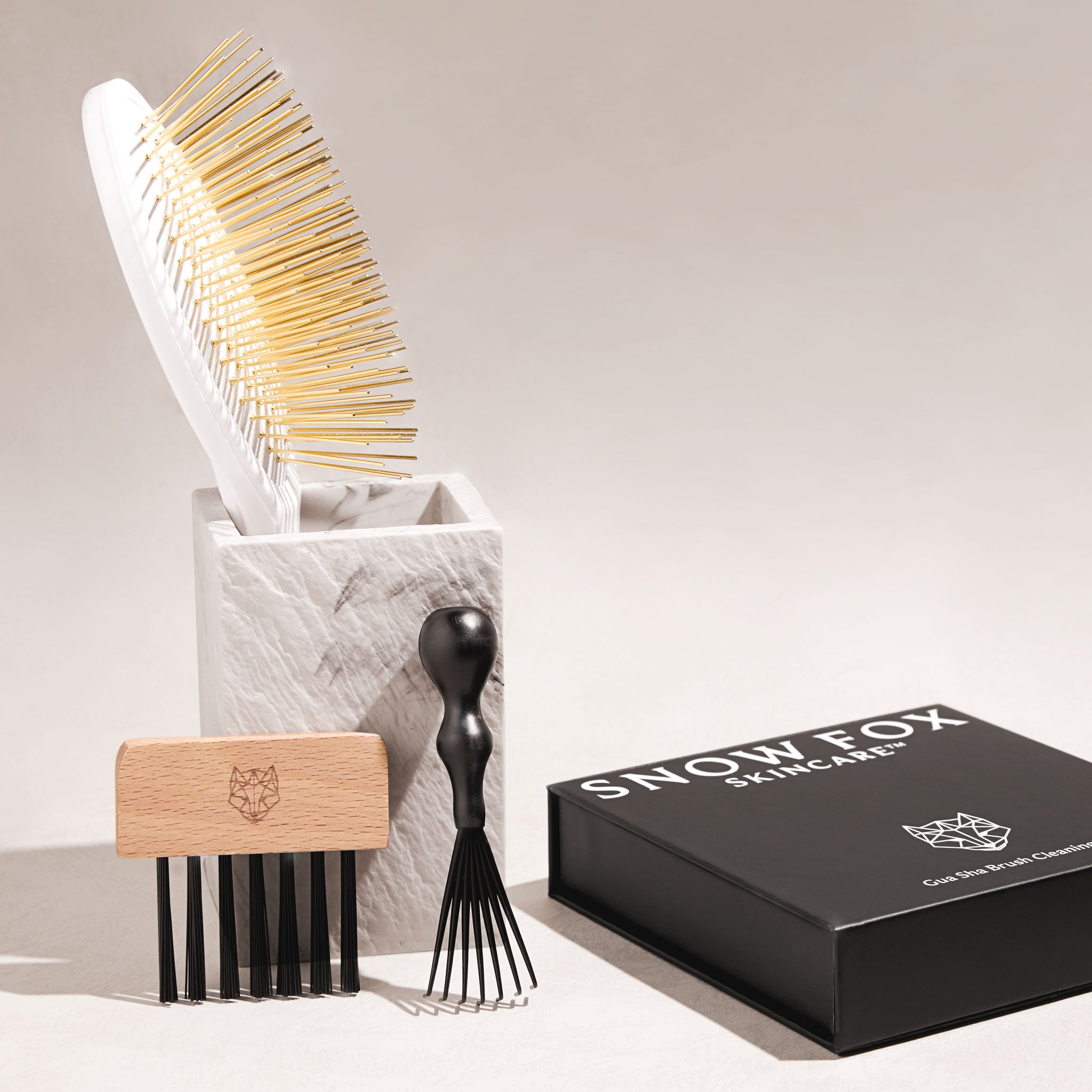 the Snow Fox Skincare Gua Sha Brush and the Gua Sha Brush Cleaning Kit with the rake brush and bristle comb for brush pad next to each other on a light beige background