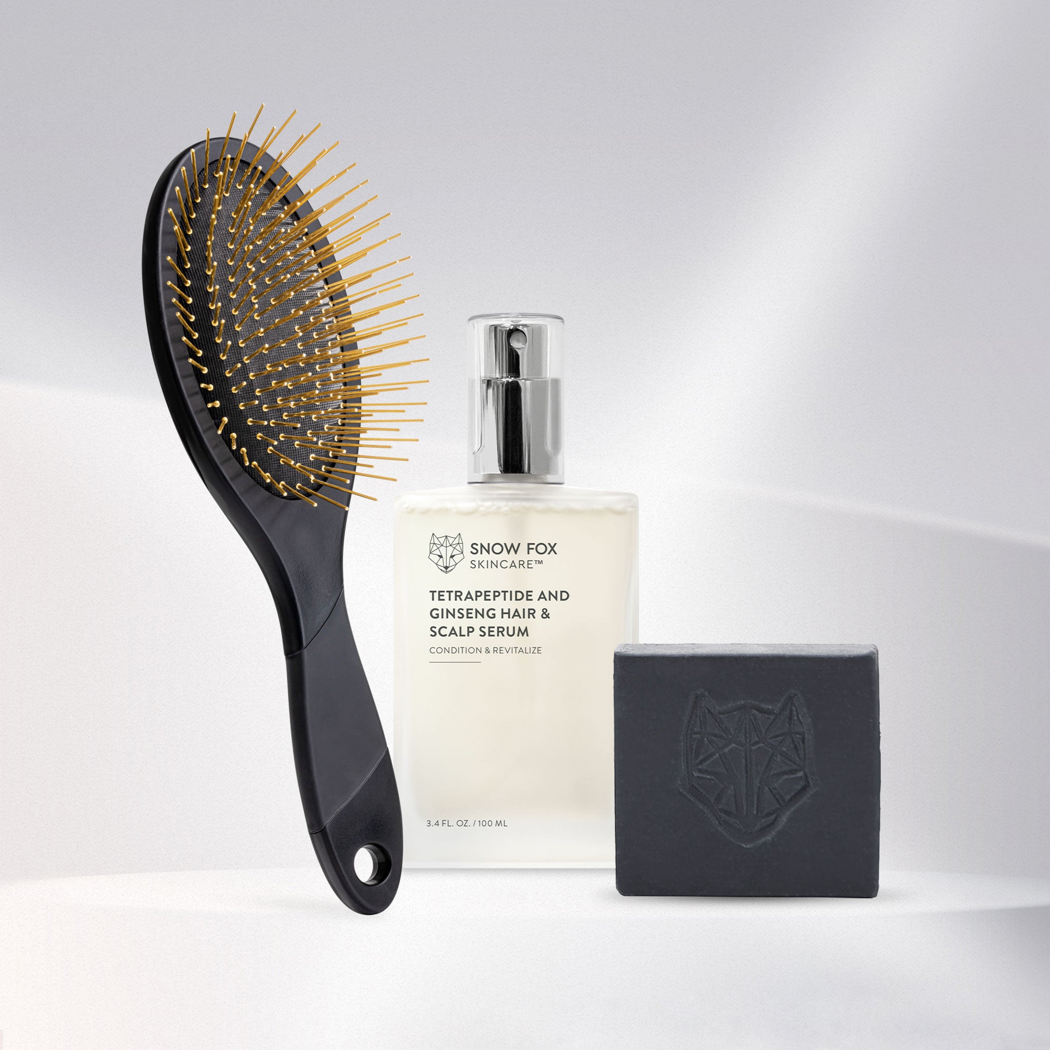 Set of Snow Fox Skincare grooming tools including a black Gua Sha brush, Hair serum bottle, and black all in one cleansing bar on a beige background