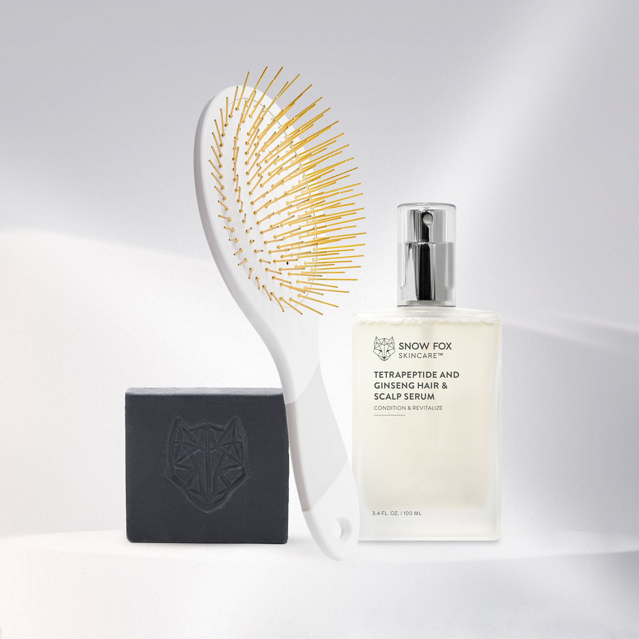 Set of Snow Fox Skincare grooming tools including a White Edition Gua Sha brush, Tetrapeptide Hair serum bottle, and black all in one cleansing bar on a beige background