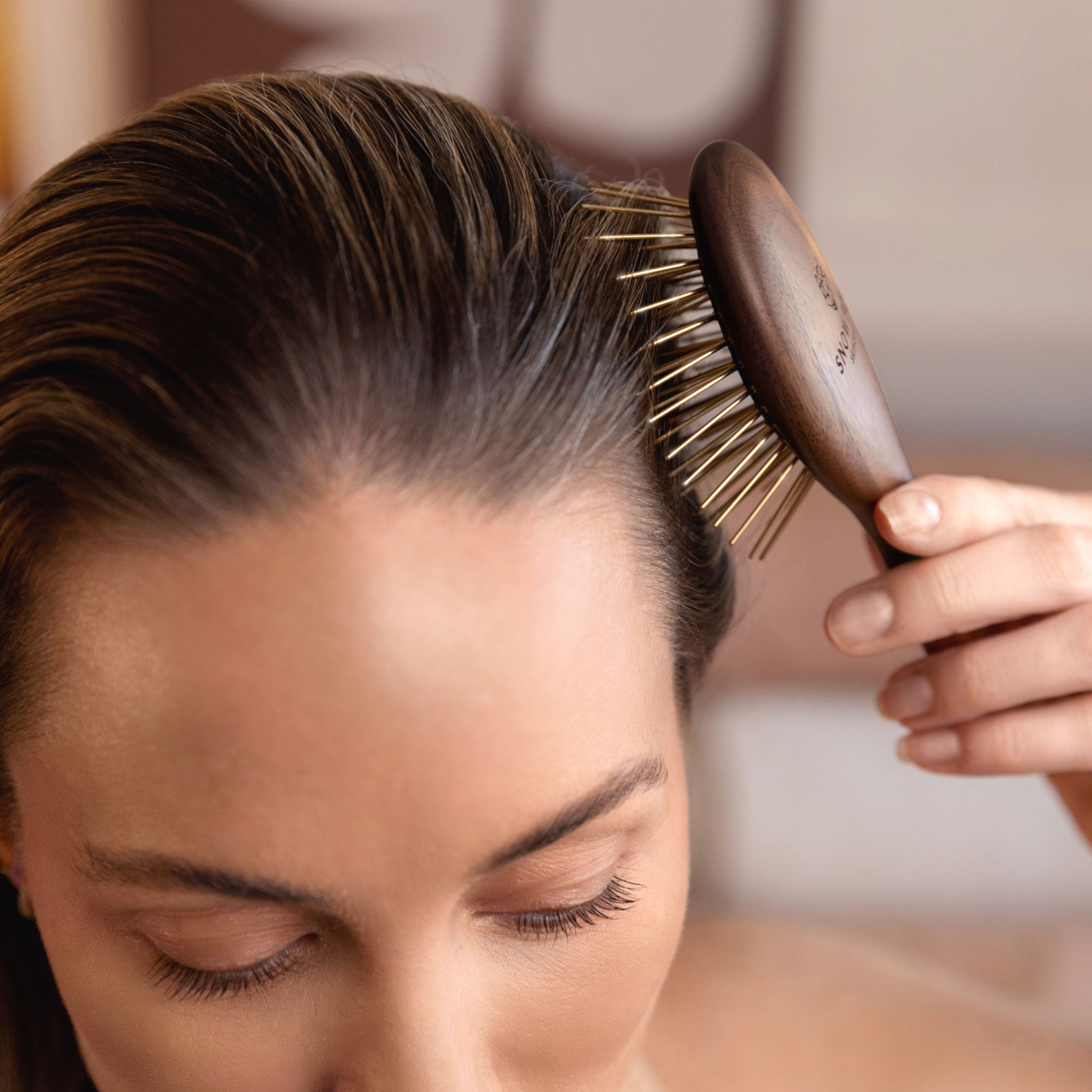 woman using the Snow Fox Skincare infrared Gua Sha hair brush on their hair with a blurred background, for thick, healthy hair