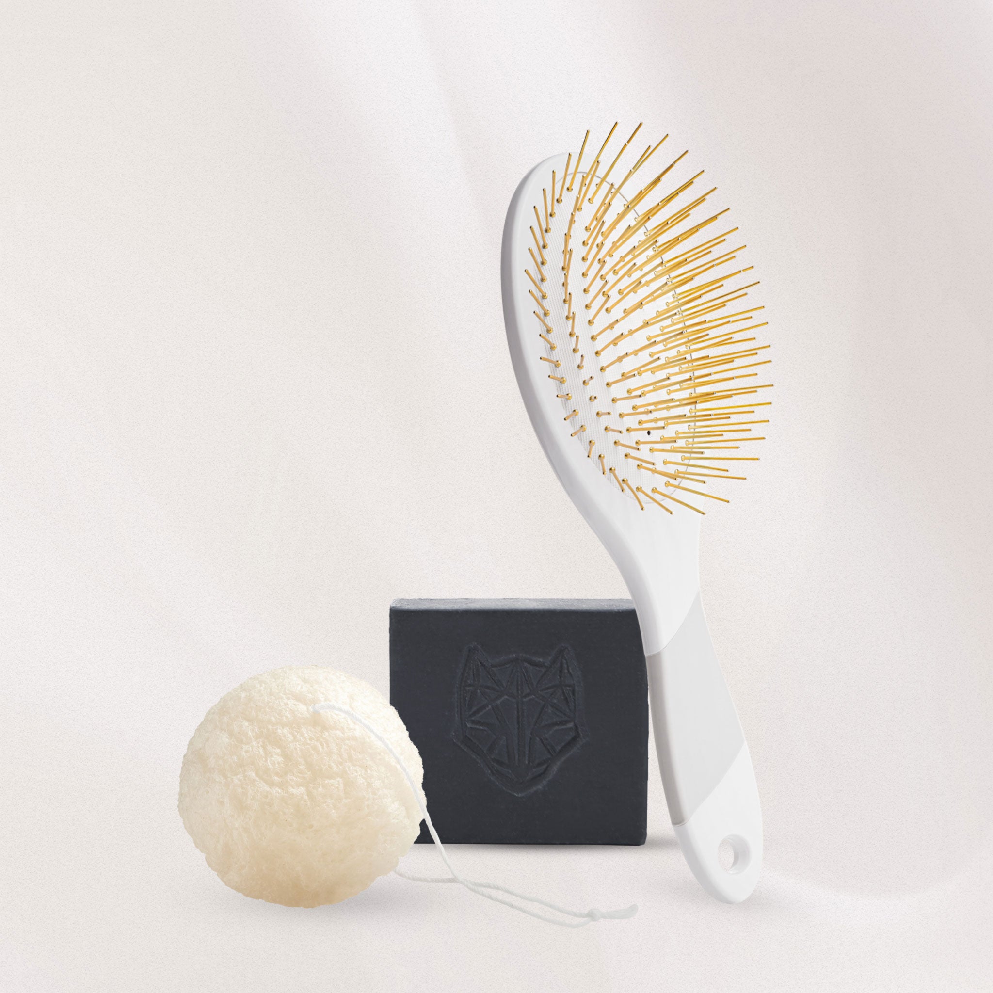 Set of Snow Fox Skincare grooming tools including a White Edition Gua Sha brush, white konjac sponge, and black all in one cleansing bar on a beige background