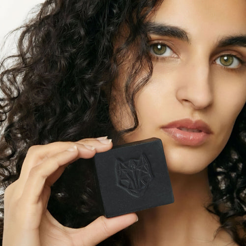 Woman holding a  Snow Fox Skincare all in one cleansing black bar with a logo close to her face
