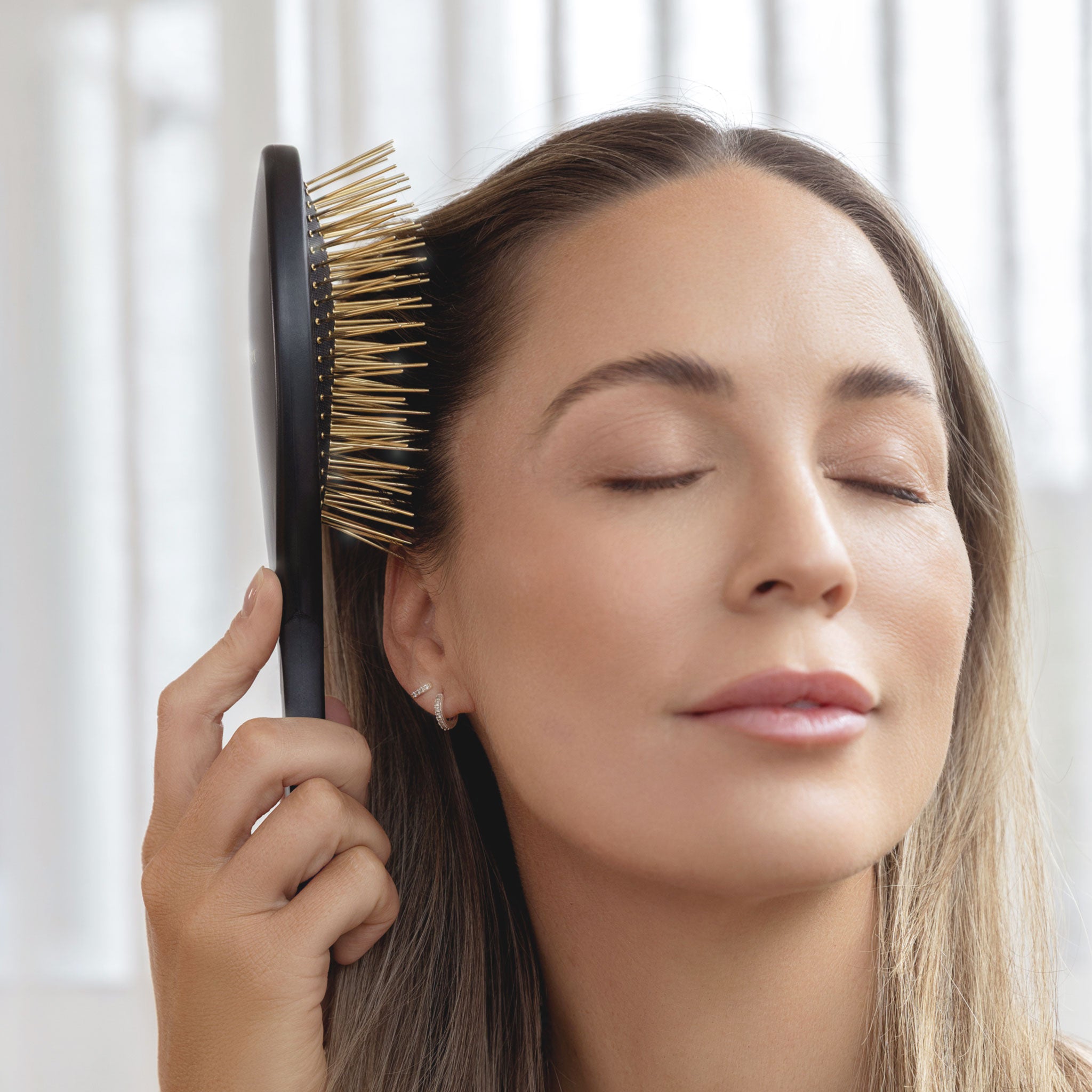 An older woman using Black Gua Sha brush by Snow Fox Skincare with black handle and gold acupressure needles in her loungeroom 