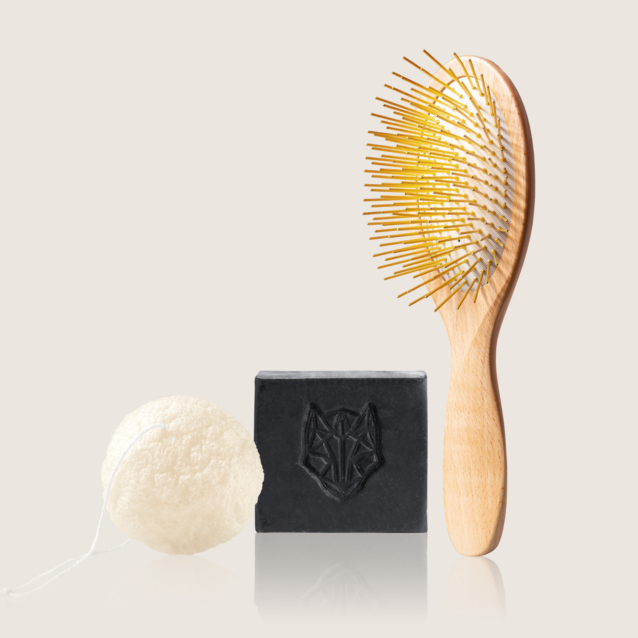 Wooden Gua Sha brush with gold acupressure needles and an all-in-one cleansing black bar by Snow Fox Skincare and Tohoku Konjac Sponge on a light beige background