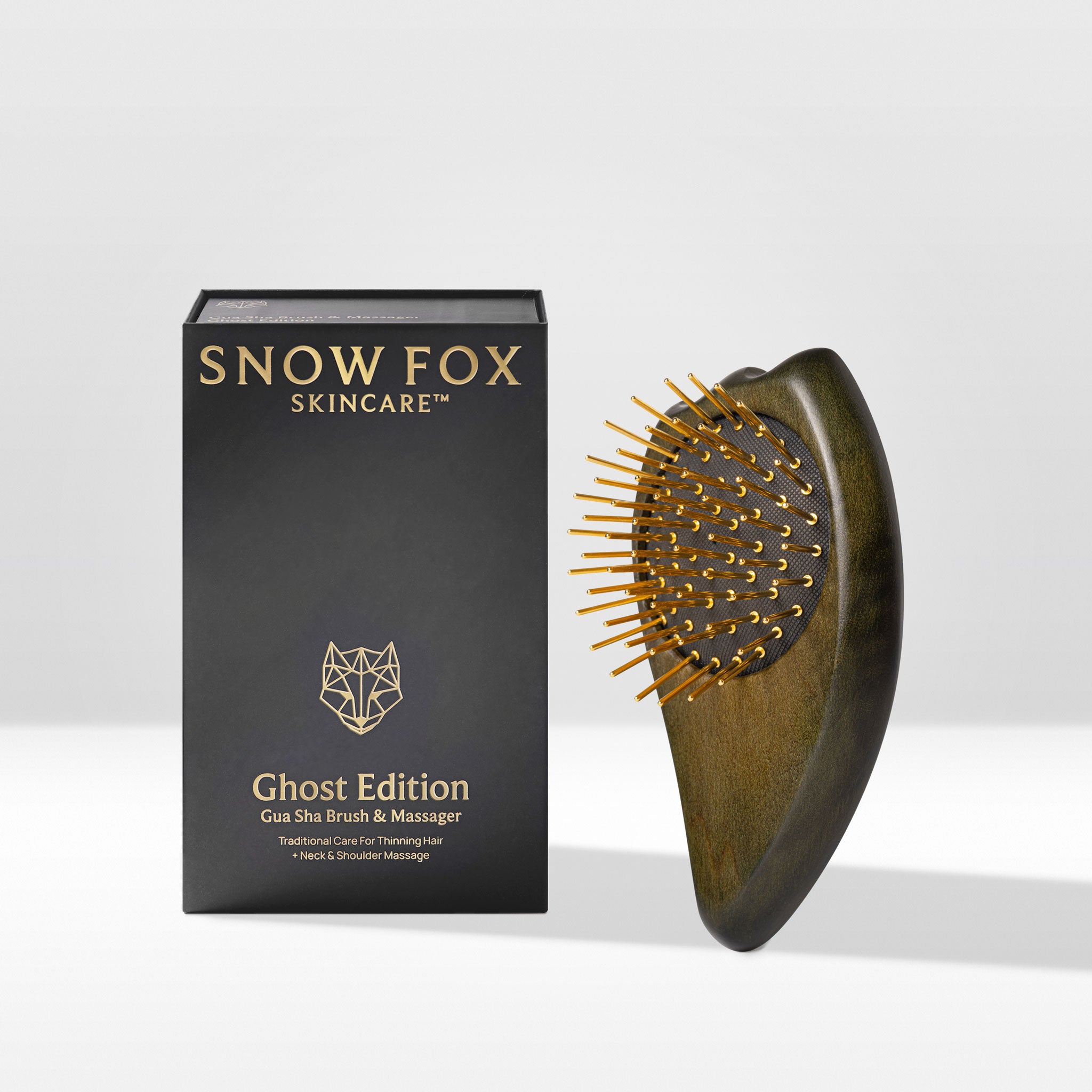 A wooden Gua Sha Brush & Massager with gold-colored acupressure needles next to its black packaging box, labeled 'Snow Fox Skincare' and 'Ghost Edition'.