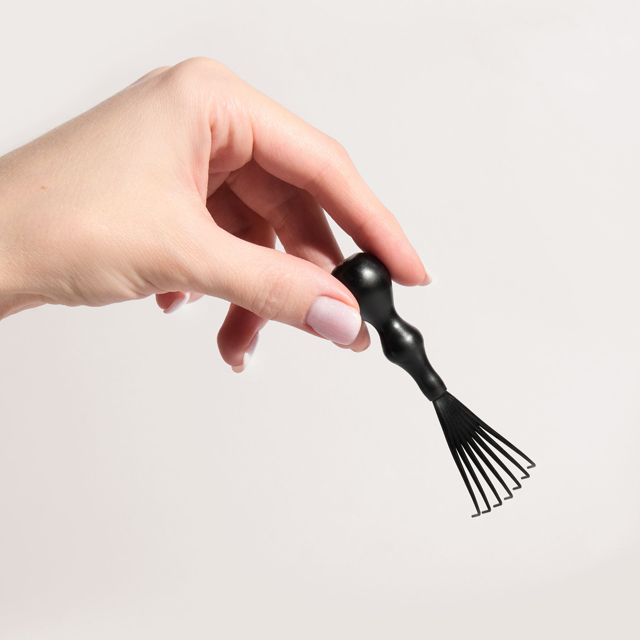 a woman's hand holding the Snow Fox Skincare Gua Sha Brush Cleaning Kit  rake brush on a light beige background 