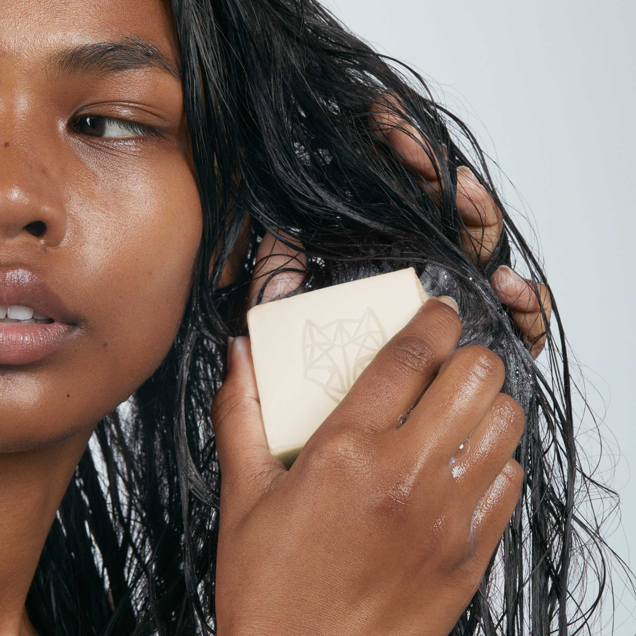 black Model with straight hair using Snow Fox Skincare hydrating hair and body cleansing bar to create a rich lather with a white background