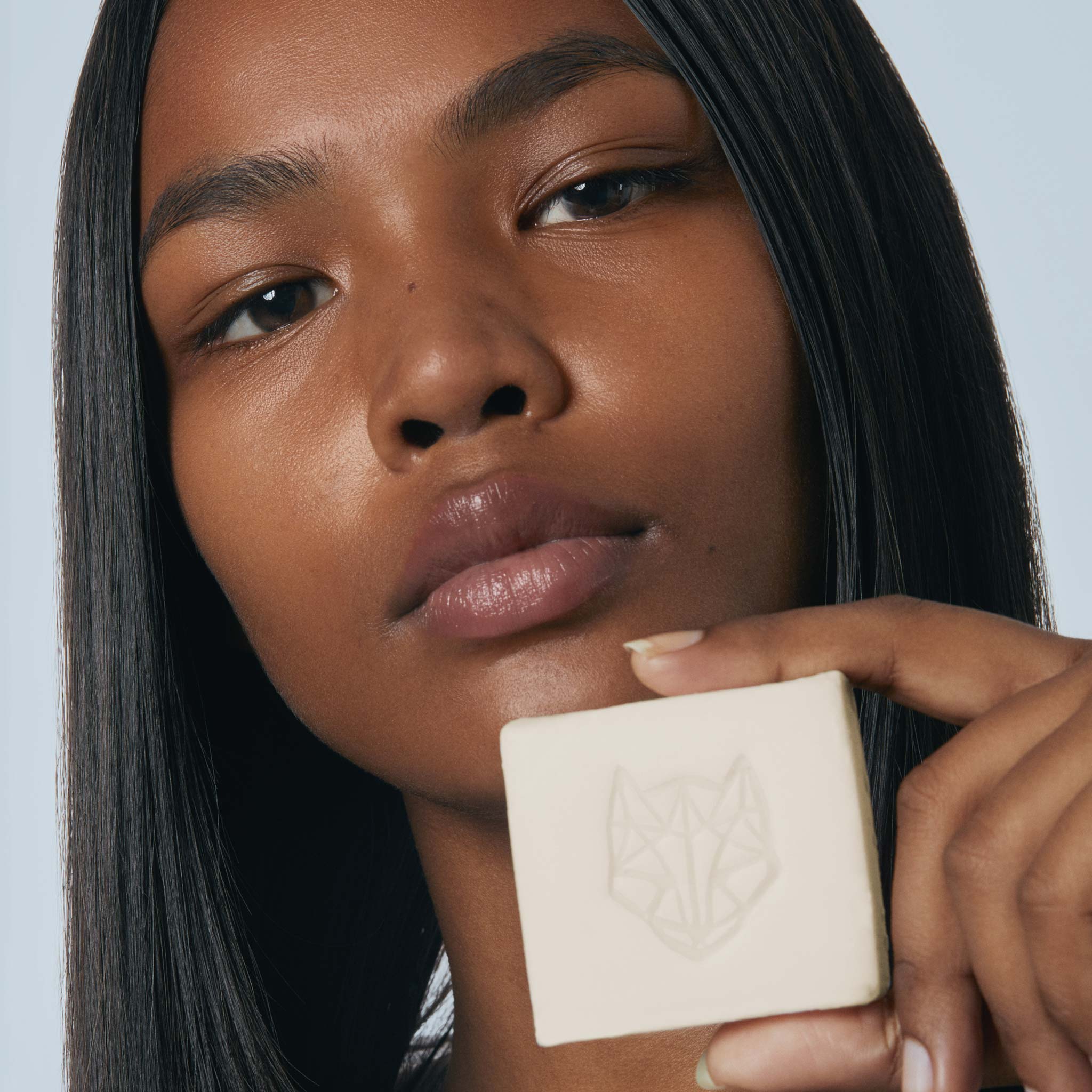 black female Model with straight hair using Snow Fox Skincare hydrating hair and body cleansing bar to create a rich lather with a white background