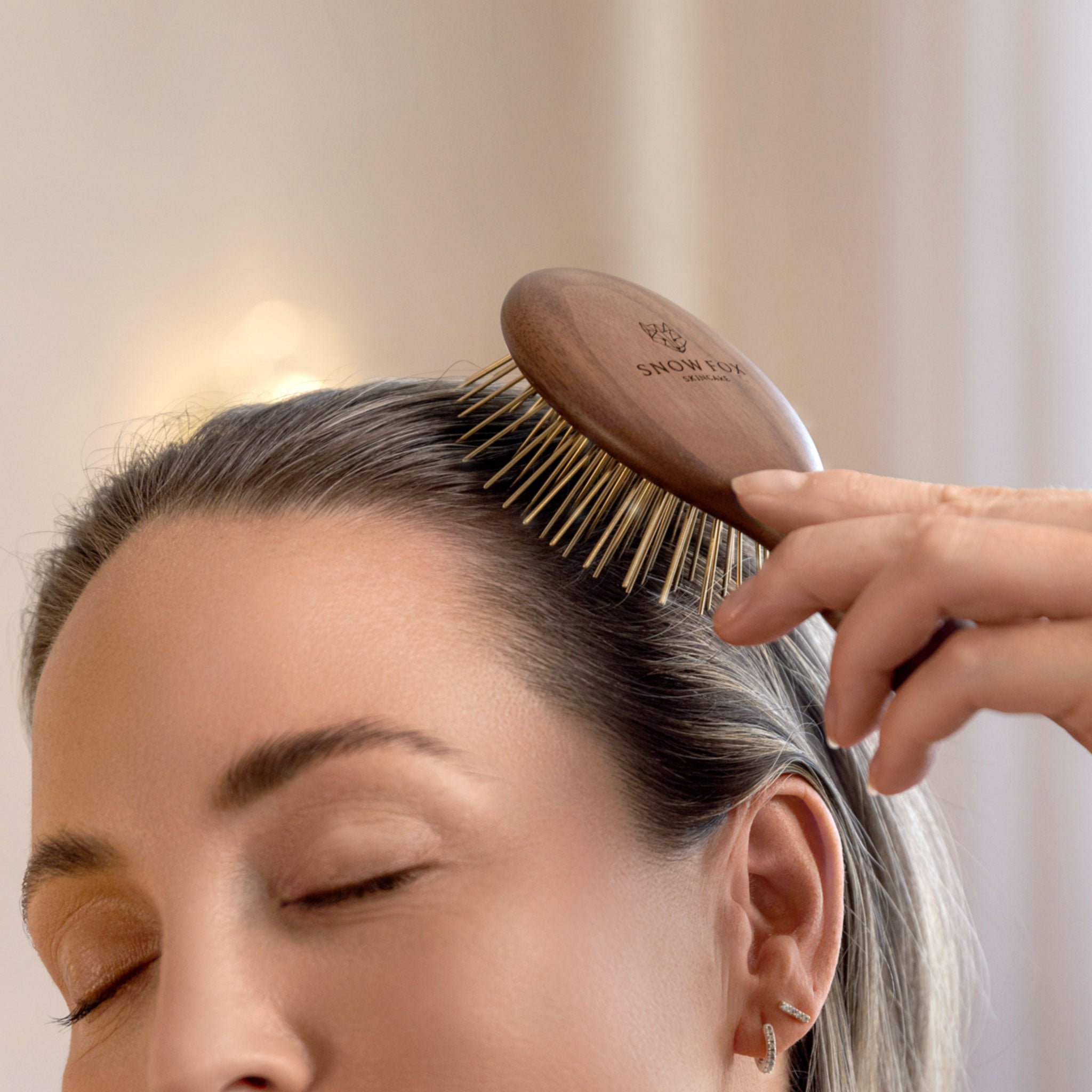 woman using the Snow Fox Skincare infrared Gua Sha hair brush on their hair with a blurred background, for thick, healthy hair