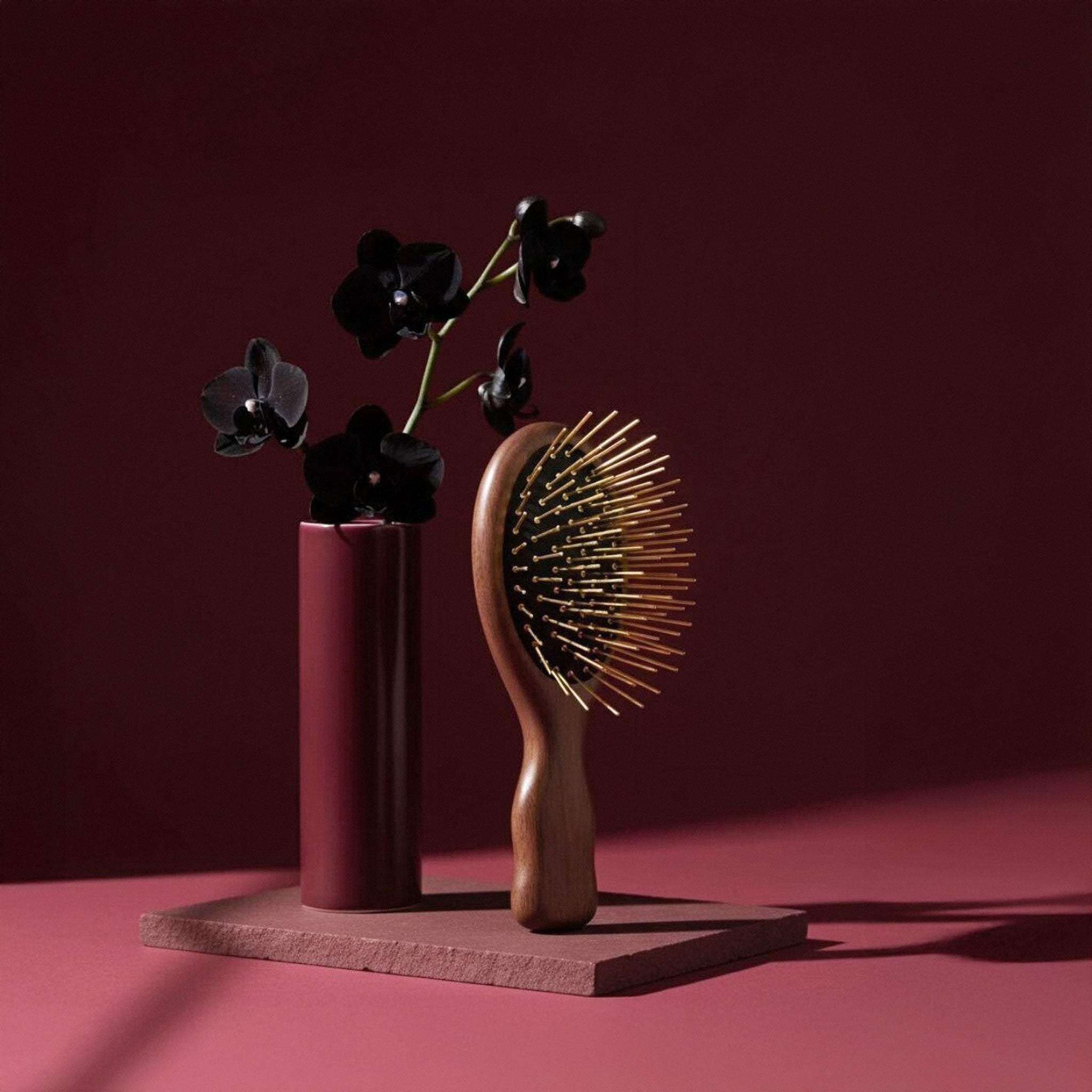 Wooden Gua Sha hairbrush and vase with black flowers on a red platform against a red background
