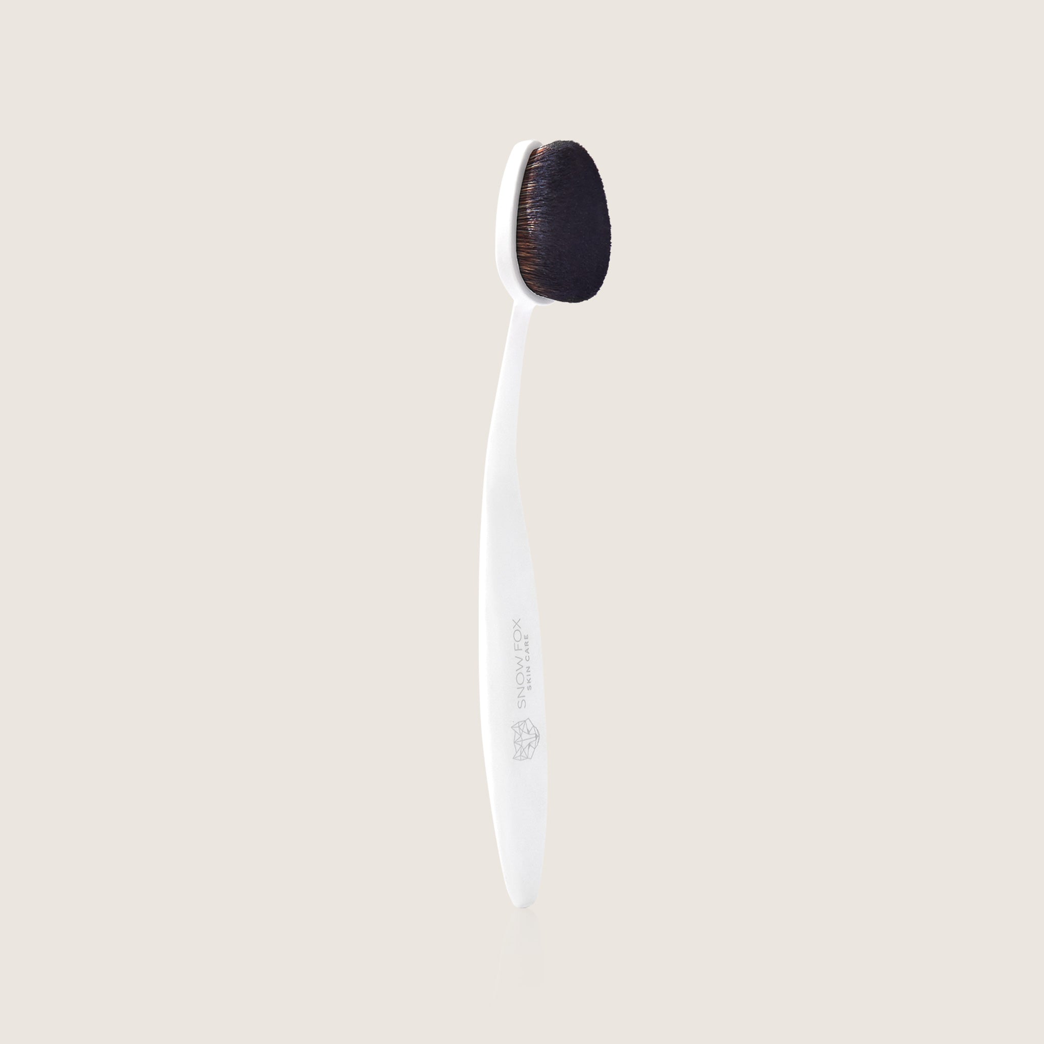 Cloud skin make up brush with black bristle head and white handle by Snow Fox Skincare on a beige background