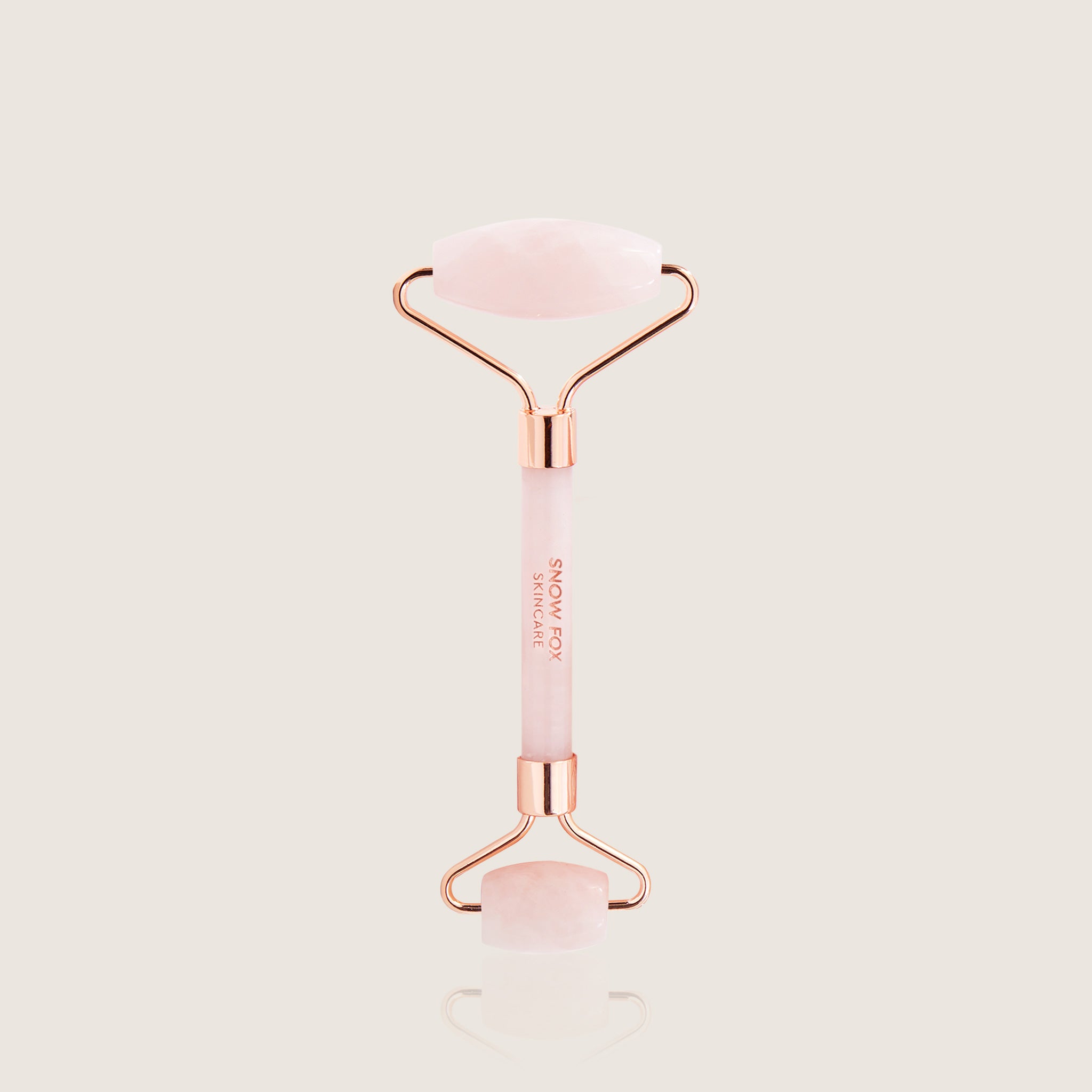 Rose gold and pink crystal facial roller on a light beige background