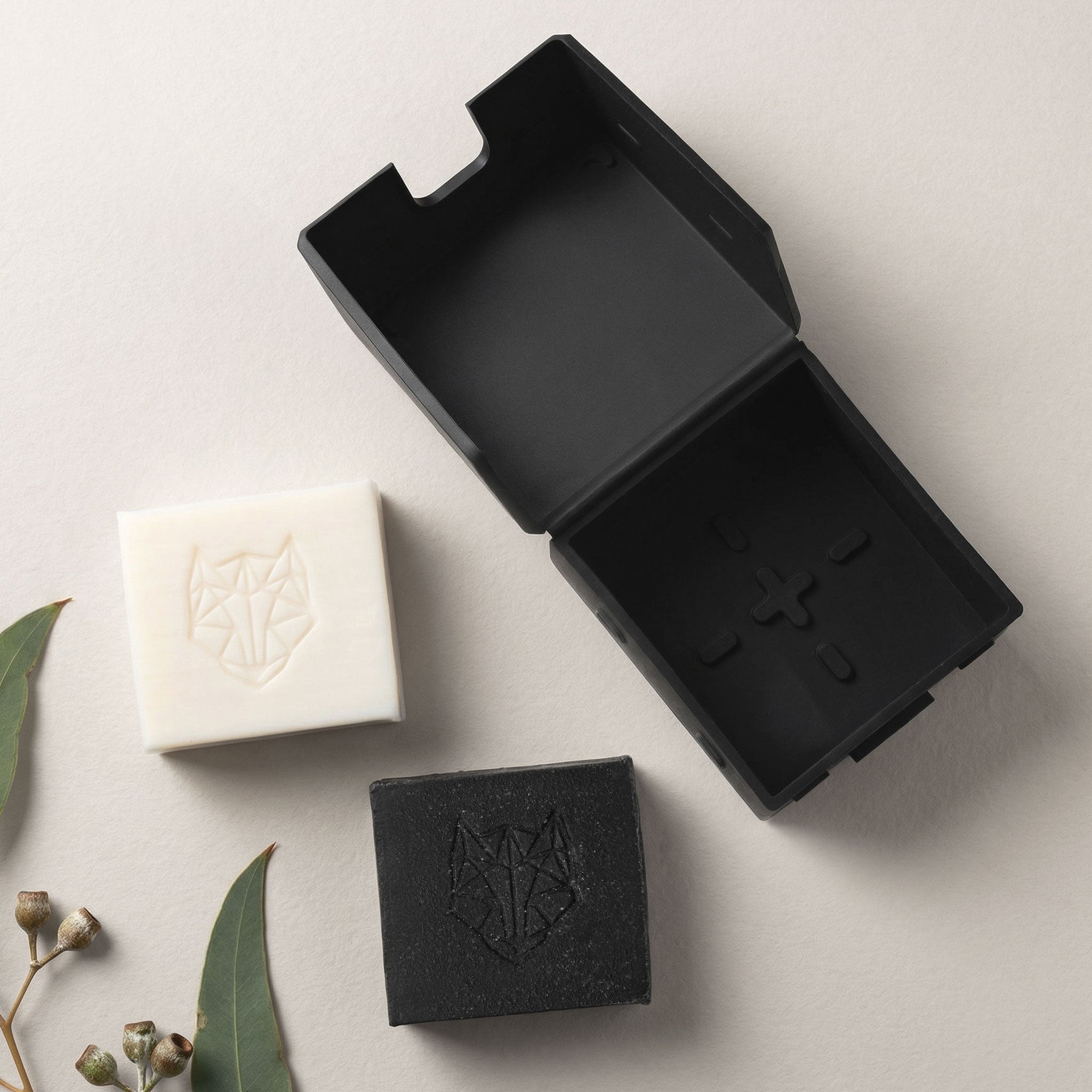 Black soap dish with two bars of soap on a light surface.