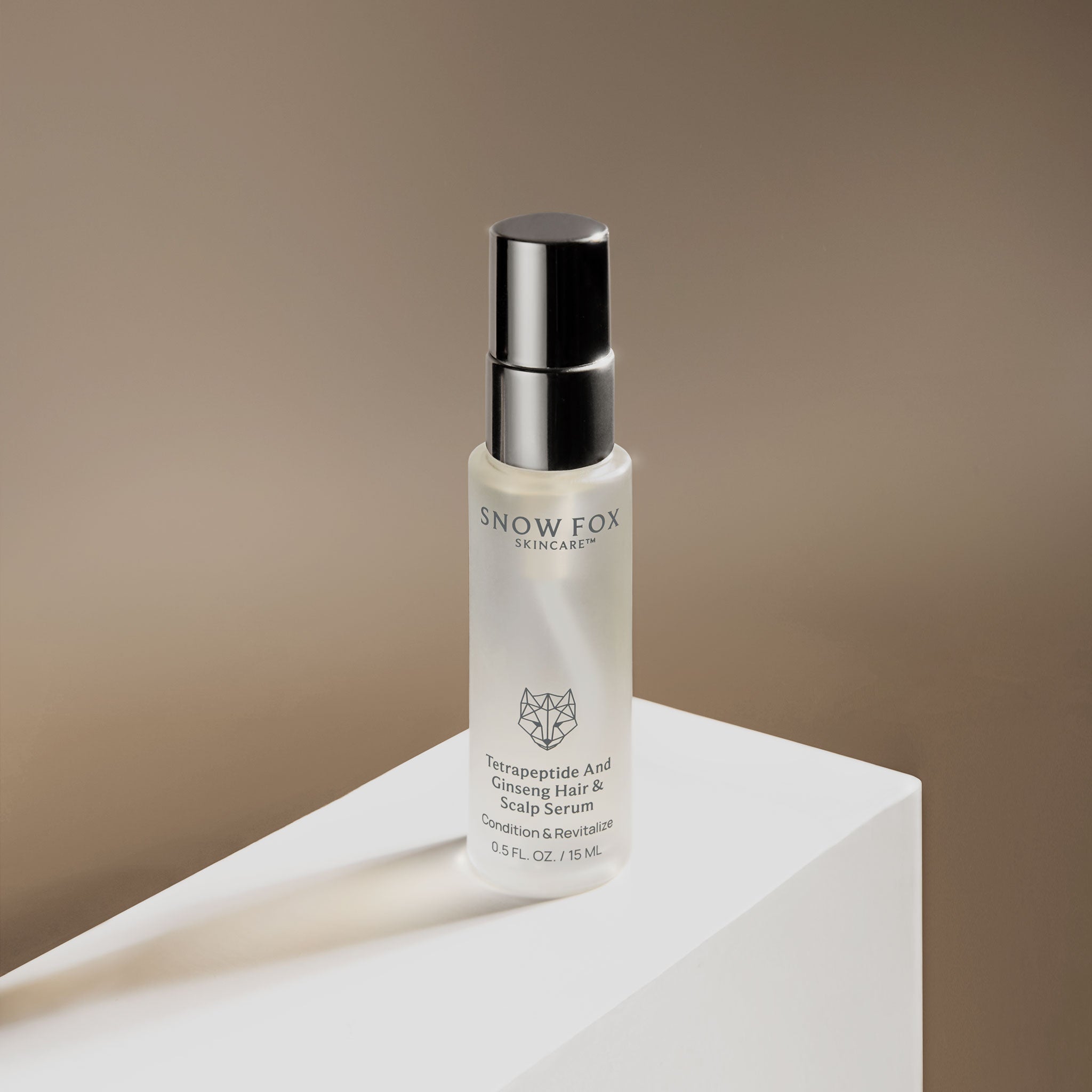 Snow Fox skincare Hair serum travel sized bottle on a white platform with a beige background