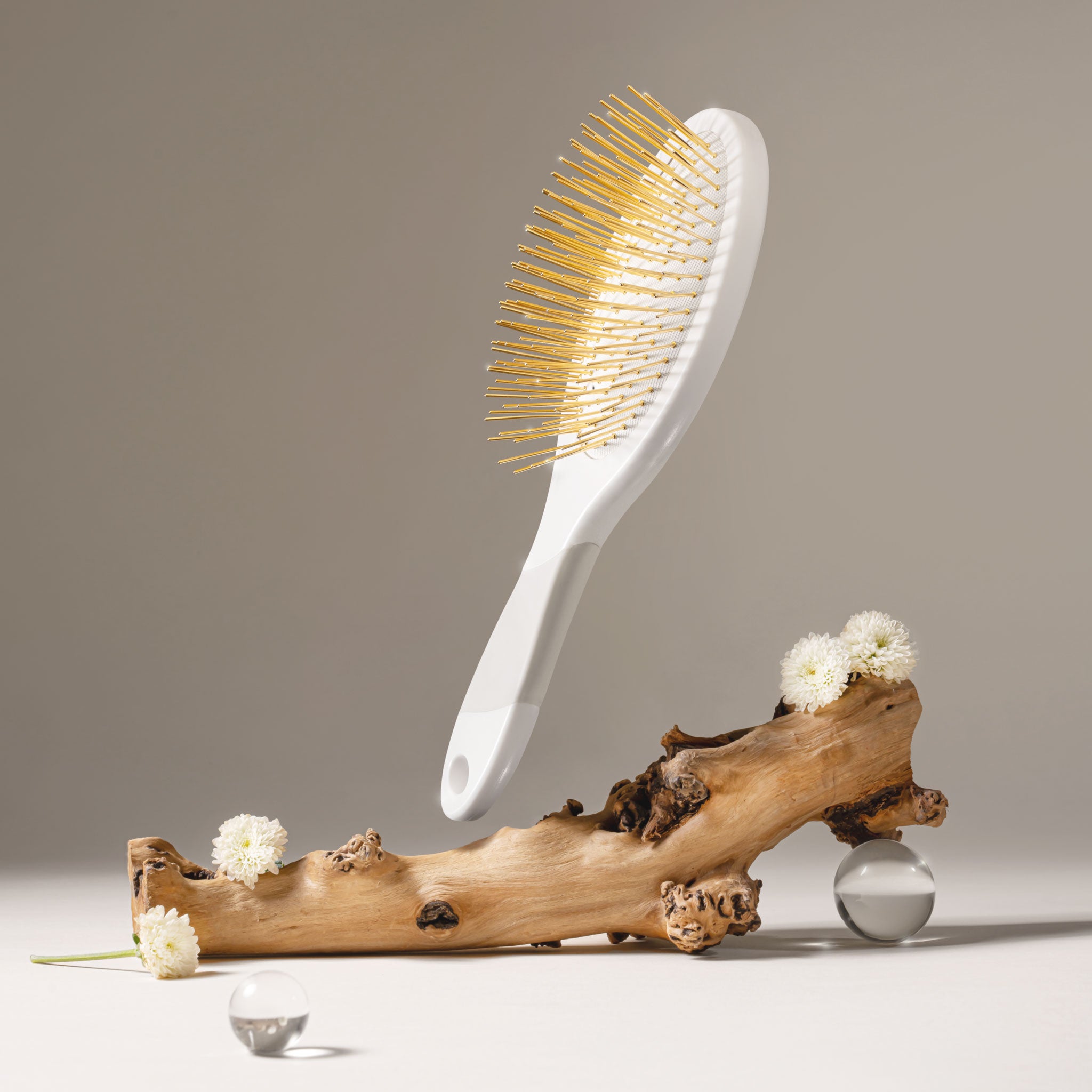 White Edition Thermoplastic Gua Sha Brush by Snow Fox Skincare on a beige background with wood branch and flowers 