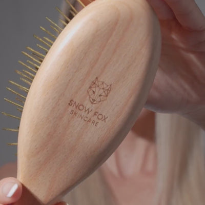 Wooden Snow Fox Skincare gua sha brush with 24k gold-plated needles being used on model with blonde hair