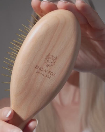 Wooden Snow Fox Skincare gua sha brush with 24k gold-plated needles being used on model with blonde hair